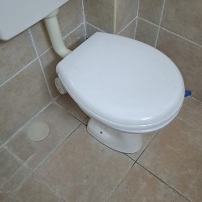 אסלה לבנה עם צינור ניקוז וקיר אריחים