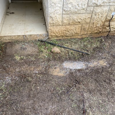 כבל חשמל שחור מחובר לקיר אבן ליד אדמה רטובה