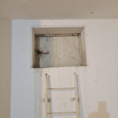 סולם מתכת מול פתח בקיר לבן