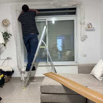 אדם על סולם מתקן תריס בחדר מגורים