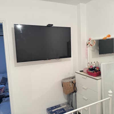 חדר עם טלוויזיה תלויה על הקיר, שידה עם מראה ומוצרי טיפוח.