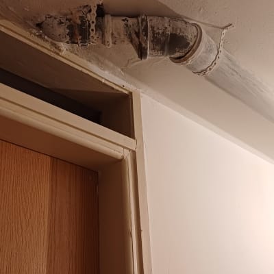 צינור מתכת עם חיבורים על תקרה ליד דלת עץ