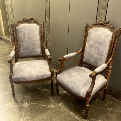 שני כיסאות מרופדים בבד אפור עם מסגרת עץ מעוטרת