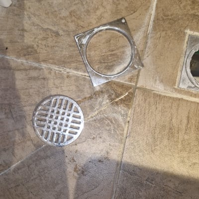 רשת ומכסה ניקוז מפורקים על רצפת חדר רחצה