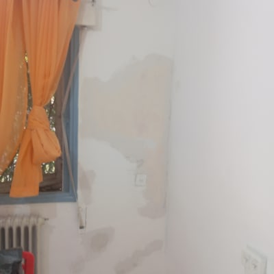 קיר עם סימני צבע ותיקונים ליד חלון עם וילון כתום