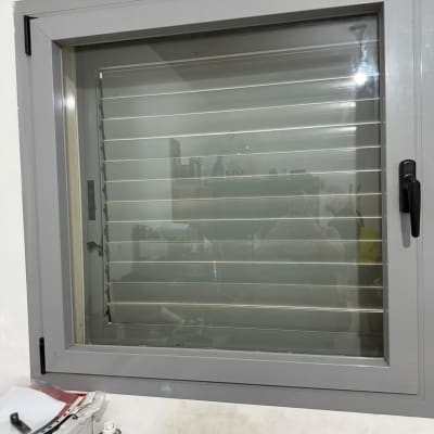 חלון עם תריסים אפורים מותקנים על קיר לבן