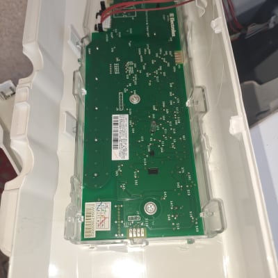 לוח מעגלים ירוק עם חוטים אדומים בתוך מארז פלסטיק לבן