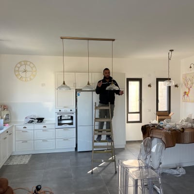 חשמלאי עומד על סולם ומתקין מנורות תקרה