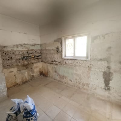 קירות חשופים עם סימני טיח, חלון, שקי חומרי בניין