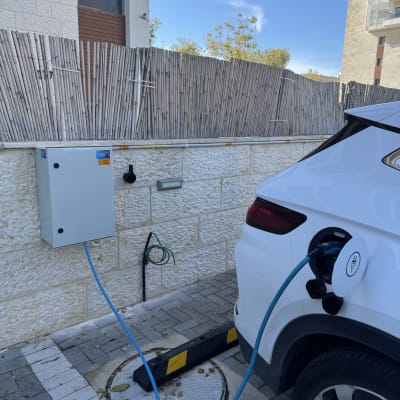 רכב חשמלי מחובר לעמדת טעינה ליד קיר חיצוני