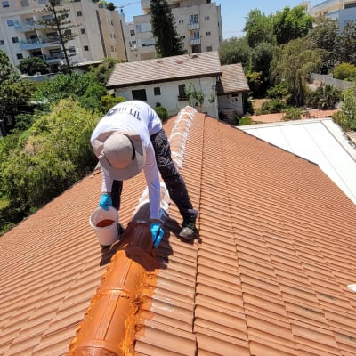 אדם מורח חומר על רעפים בגג רעפים