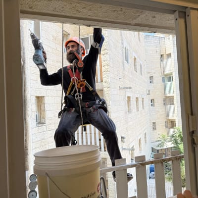 אדם עם קסדה ורתמה מחזיק מקדחה ליד חלון