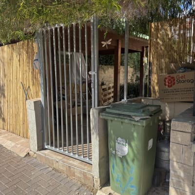 שער מתכת ליד פח אשפה ירוק