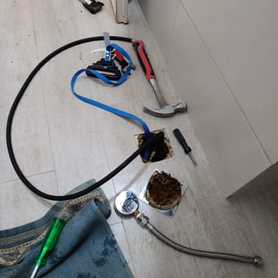 כלי עבודה של אינסטלטור על רצפה, כולל פטיש וצינור גמיש