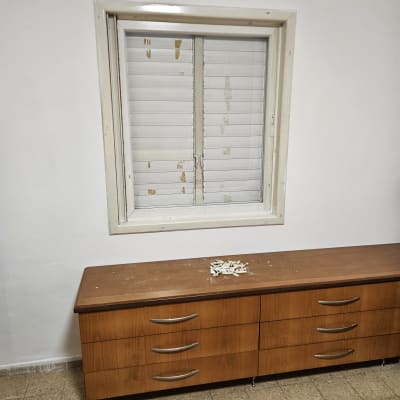 תריסים לבנים עם סימני בלאי מעל שידה חומה