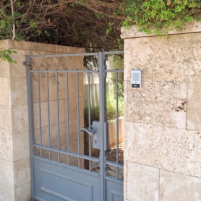 קודן כניסה אלקטרוני המותקן על קיר אבן לצד שער מתכת