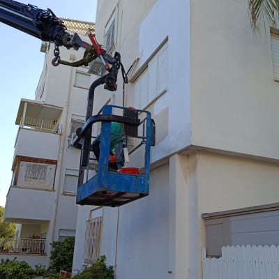 עובד בגובה על מנוף צובע קיר בניין
