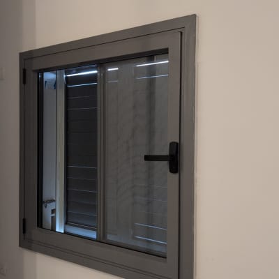 חלון עם תריסים אפורים מותקנים על קיר לבן