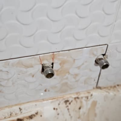 צינורות מים חשופים בקיר עם אריחים לבנים