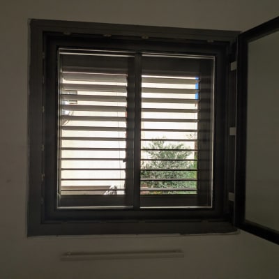 חלון ציר מאלומיניום בגוון אפור כהה עם תריס שלבים מותקן בחדר