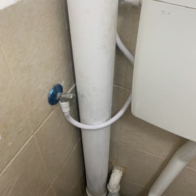 צינור מים לבן עם ברז כחול על קיר אריחים