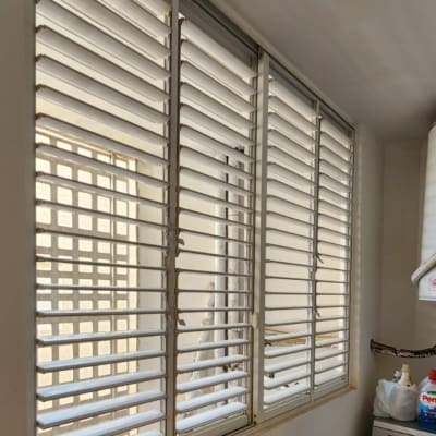 תריסים לבנים על חלון בחדר עם מכונת כביסה