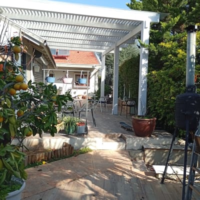 פרגולה לבנה בגינה עם עציצים ועצים מסביב