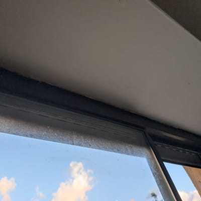 חלון עם תריסים פתוחים חלקית, שמיים כחולים עם עננים