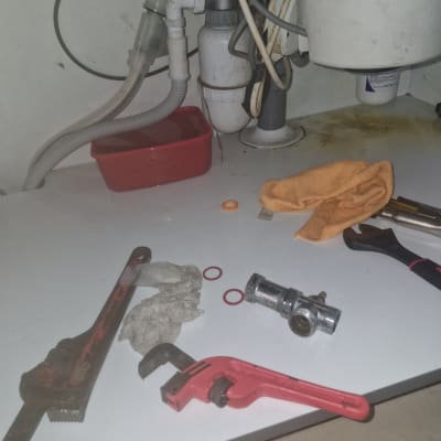 כלים וחלקים מתחת לכיור, כולל מפתח צינורות ואטמים