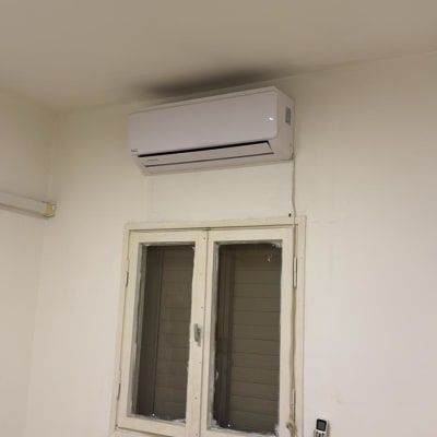 מזגן מותקן על קיר מעל חלון עם שלט רחוק