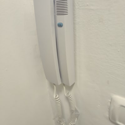 אינטרקום לבן עם כפתור כחול על הקיר