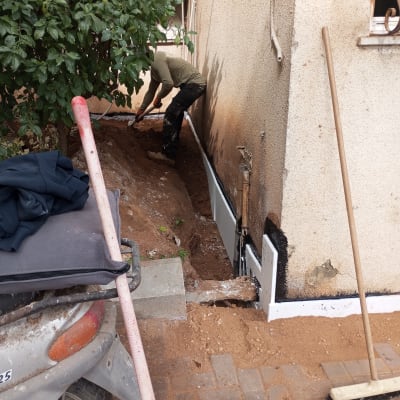 אדם עובד על איטום קיר חיצוני עם חומר שחור