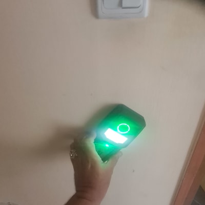 יד מחזיקה מכשיר מדידה על קיר עם מתג חשמל