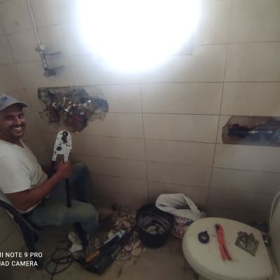 אדם מחזיק כלי עבודה ליד קיר עם צנרת חשופה