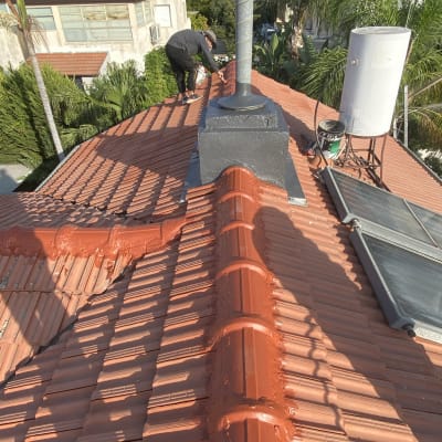 אדם עובד על גג רעפים עם צינור ומיכל מים