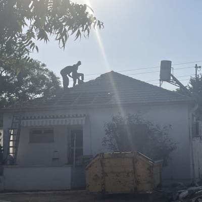 אדם עובד על גג בית עם סולם ומיכל מים