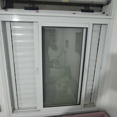 חלון עם תריס גלילה פתוח מעל מיטה ורודה