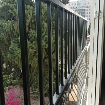 מעקה מתכת שחור במרפסת עם נוף עצים ברקע