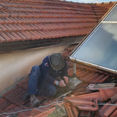אדם מתקן רעפים על גג רעפים אדום