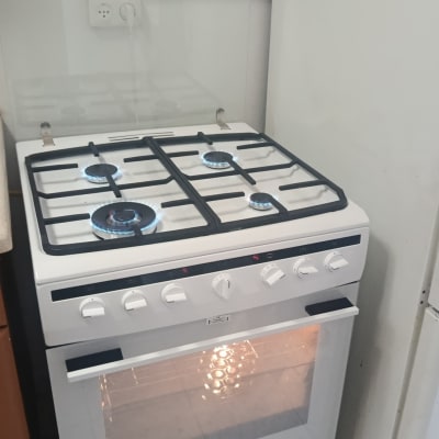 תנור גז לבן עם כיריים דולקות במטבח