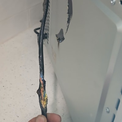 כבל חשמלי שרוף מוחזק ביד ליד מכשיר חשמלי