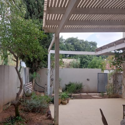 גינה עם עצים וצמחים ליד פרגולה