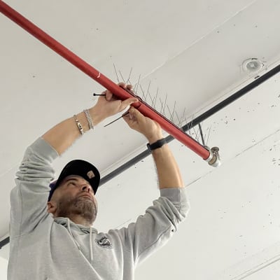 אדם מתקין דוקרנים על צינור אדום בתקרה