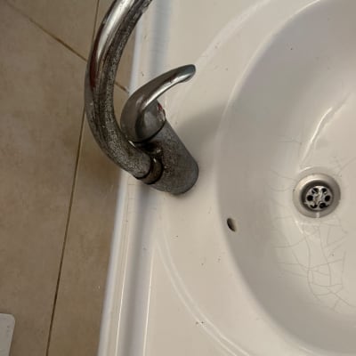 ברז מים ישן ובלוי מותקן על כיור רחצה לבן