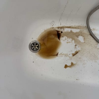 אמבטיה מוכתמת ובלויה עם מים עכורים ליד הניקוז לפני חידוש