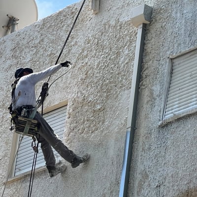 אדם עובד בגובה על קיר בניין עם חבלים