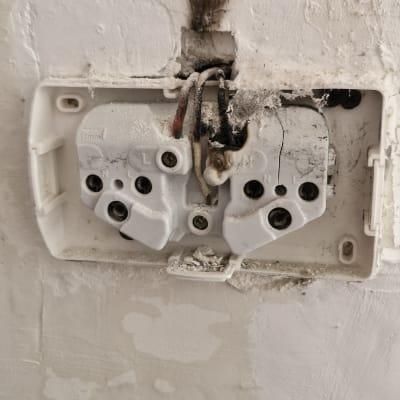 שקע חשמלי עם חוטים חשופים וקיר פגום
