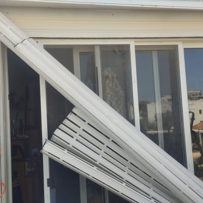 תריסים לבנים שבורים תלויים על חלון זכוכית