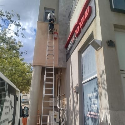 אדם על סולם צובע קיר חיצוני של בניין