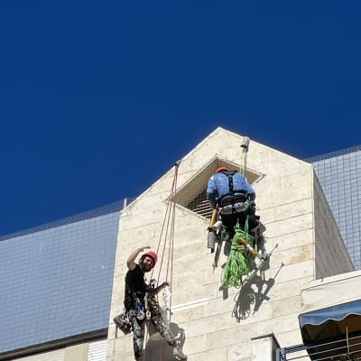 שני עובדים תלויים על חבלים על קיר בניין